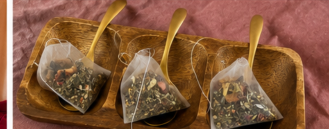 Pyramid ritual tea sachets on a wooden tray with gold spoons